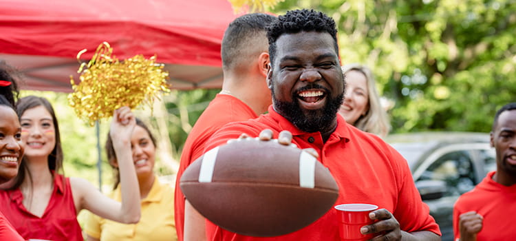 A football fan cheers at a tailgate, football in hand